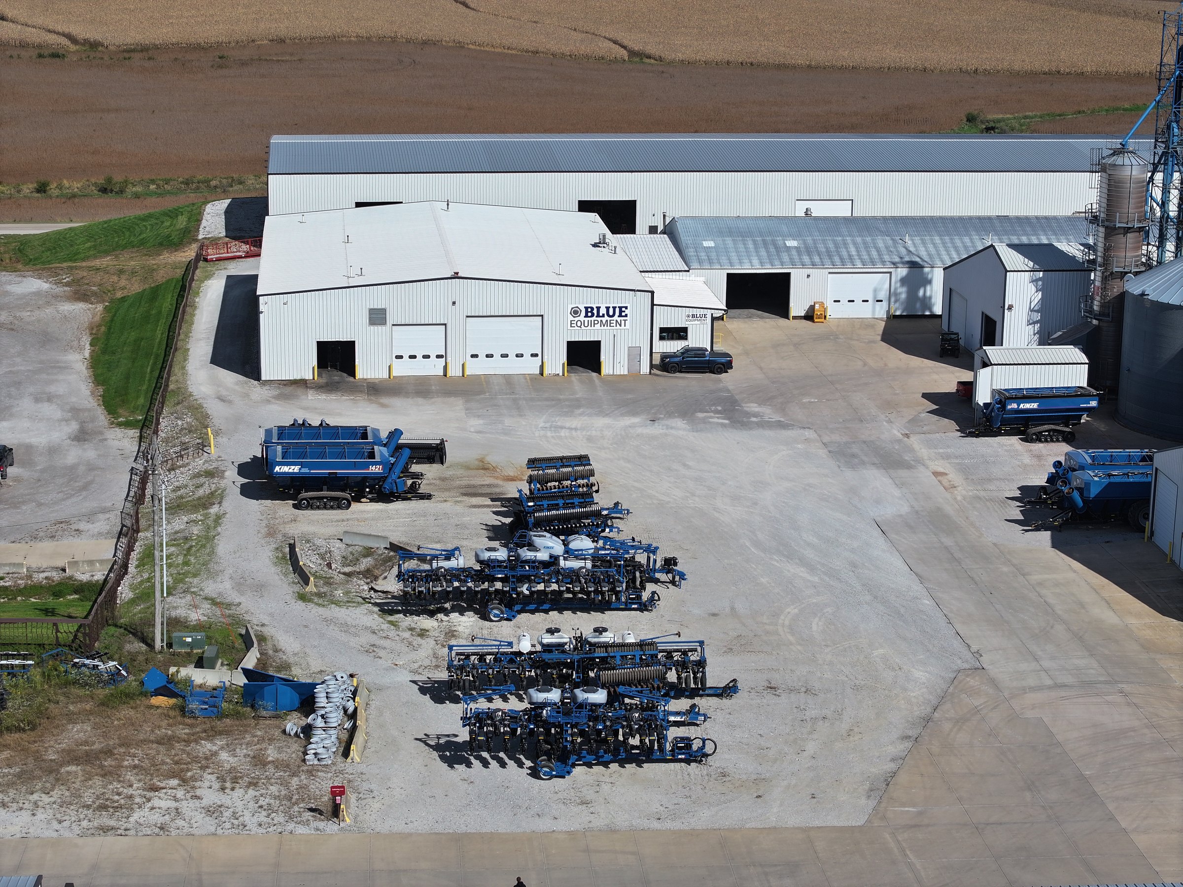 Kinze planters and grain carts on the Blue Equipment lot, with the shop behind