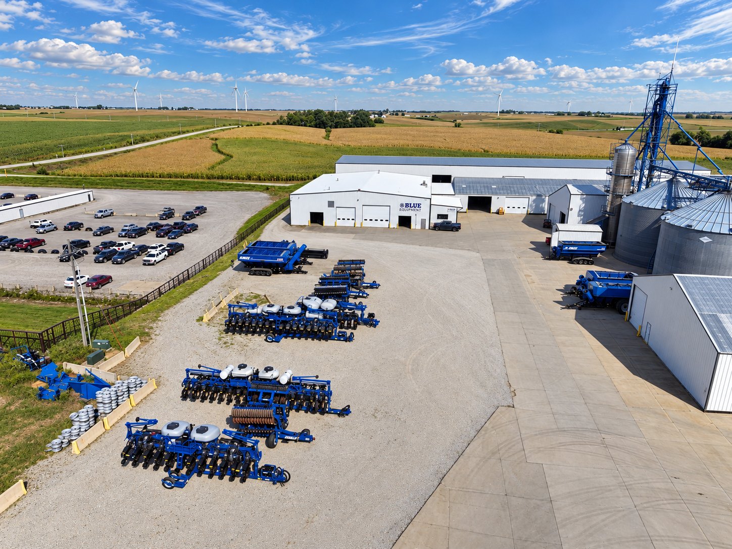 The Blue Equipment lot from above: Kinze planters, tillage tools and grain carts beside the shop and grain bins, with farm fields beyond